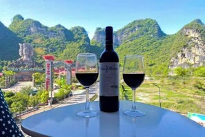 Une bouteille de vin et deux verres sur une table, avec vue sur le parc Guilin Romance et les montagnes.