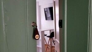A room with a door, a television mounted on the wall, and a chair. - Apartment 1 Marktkirchhof - Hotel Theophano (Quedlinburg)