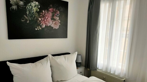 A neatly made bed with white linens, a dark headboard, and a nightstand with a lamp. - Apartment 1 Marktkirchhof - Hotel Theophano (Quedlinburg)