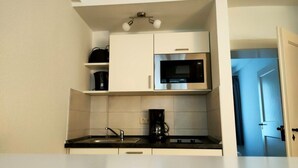 A compact kitchen with white cabinets, a built-in microwave, a coffee maker, and a sink. - Apartment 1 Marktkirchhof - Hotel Theophano (Quedlinburg)