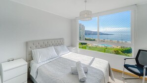 Une chambre à coucher comprenant un lit, une table de chevet, une chaise et une grande fenêtre donnant sur un paysage urbain et l’eau.