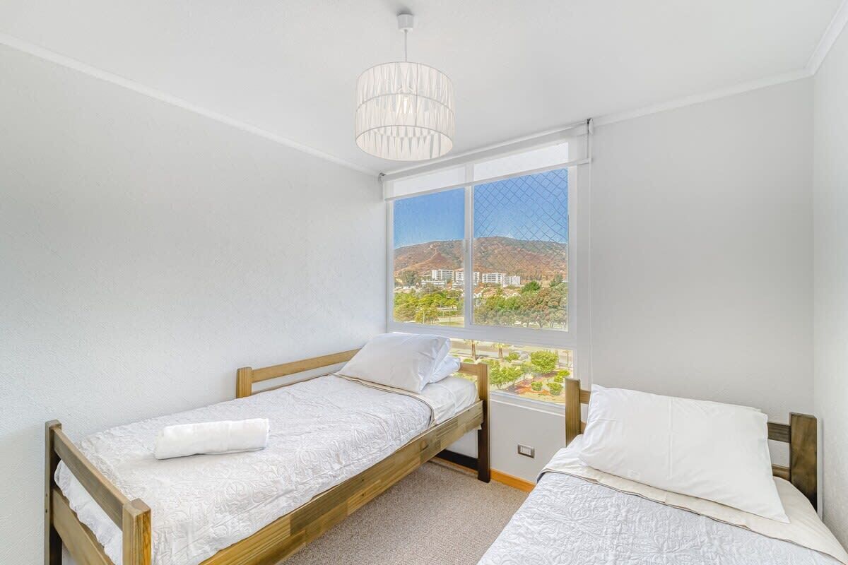 Une chambre avec deux lits simples, une grande fenêtre donnant sur un paysage urbain et un luminaire suspendu.