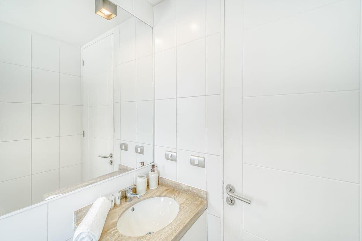 Un bagno moderno con piastrelle bianche, un lavandino, uno specchio e un asciugamano.