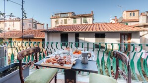 Ein Balkon mit Frühstückstisch, einschließlich Gebäck und einer Kaffeekanne, mit Blick auf eine Wohngegend mit Terrakotta-Dachziegeln und traditioneller Architektur.
