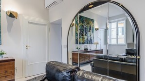 Ein modernes Wohnzimmer mit einer Ledersofa, einer Spiegelwand und einem durch den Spiegel sichtbaren Küchenbereich.