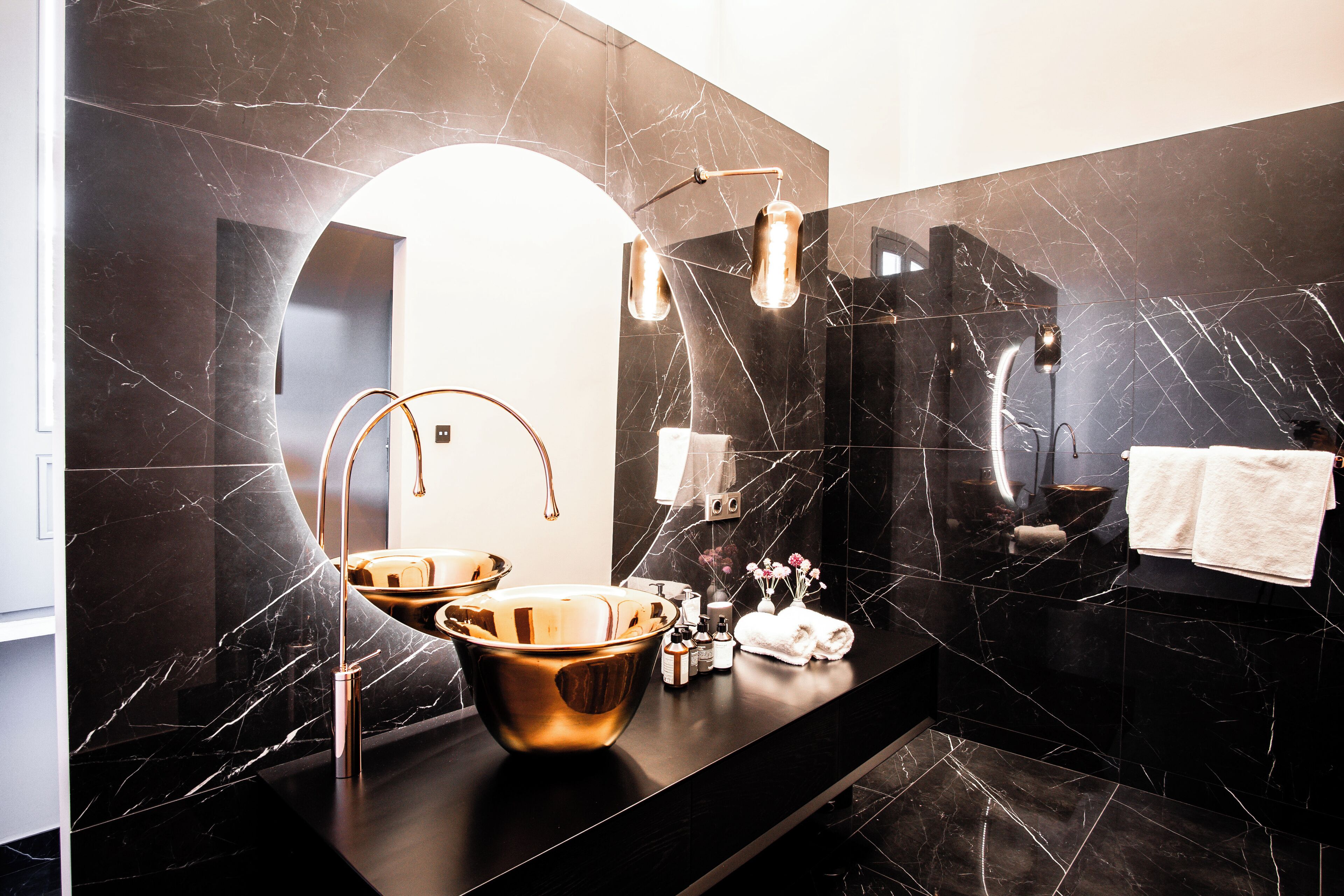 A modern bathroom with a black marble vanity, a large mirror, and a gold basin.