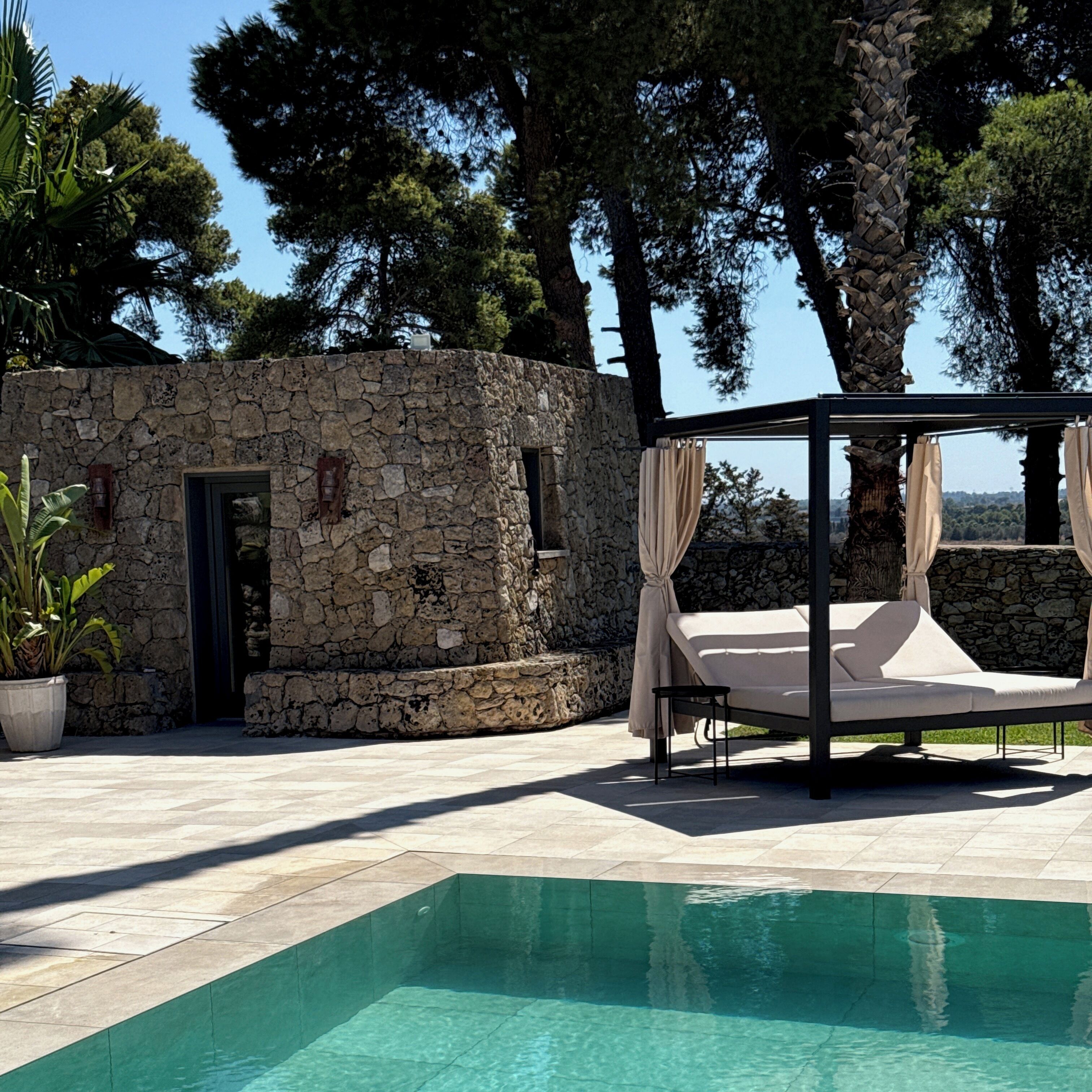A stone building with a pool, a canopy bed, and a potted plant.