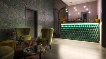 A bar area with a green neon-lit counter, a floral wallpapered wall, and a seating area with a round table and two armchairs.