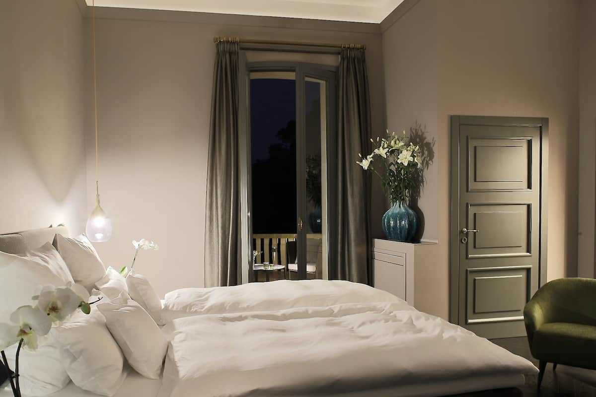 Un dormitorio con cama, mesita de noche, un jarrón con flores, una silla y una puerta.