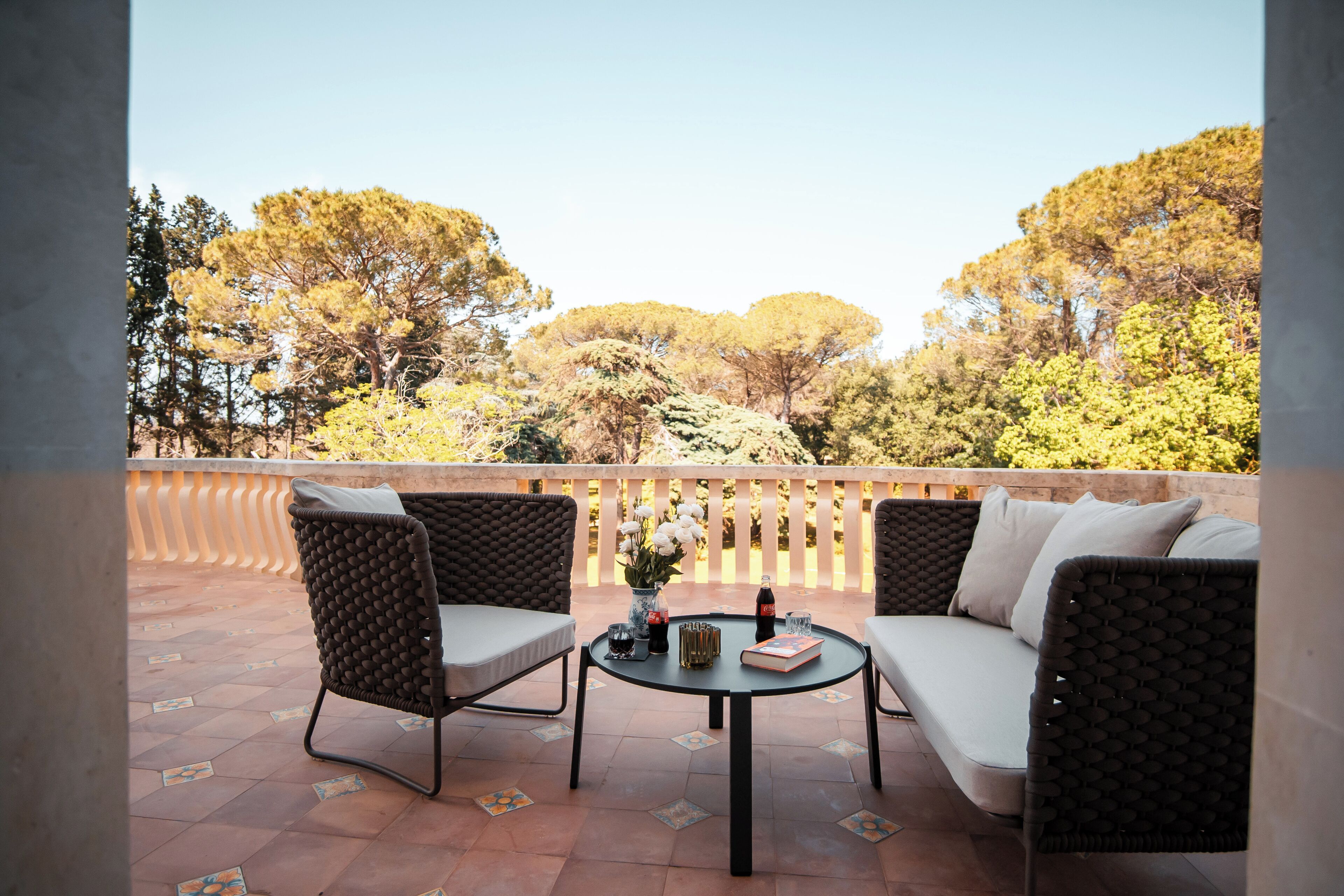 A terrace with wicker furniture, a table, and a view of trees.