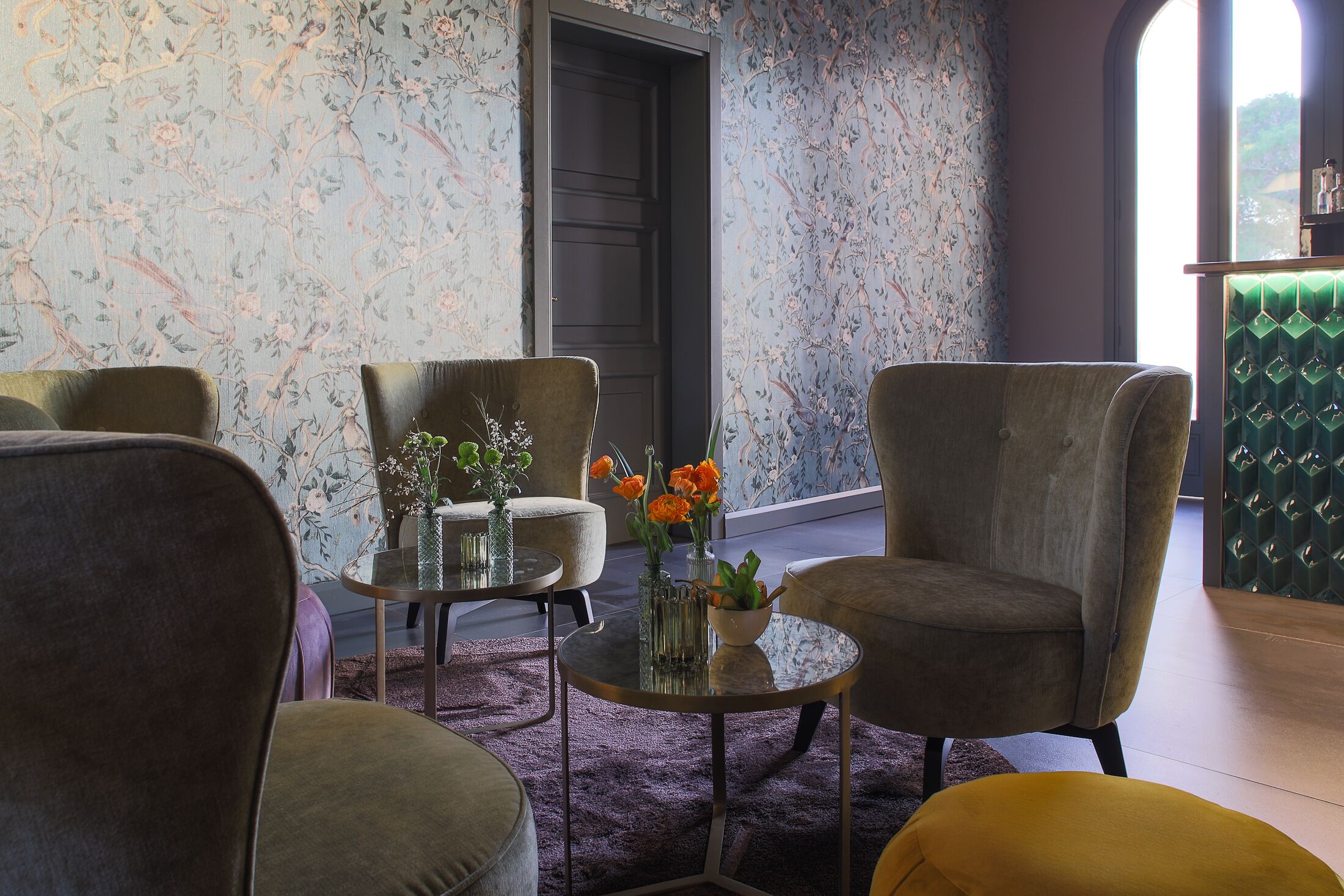 A room with floral wallpaper, a dark door, and a green upholstered bench.