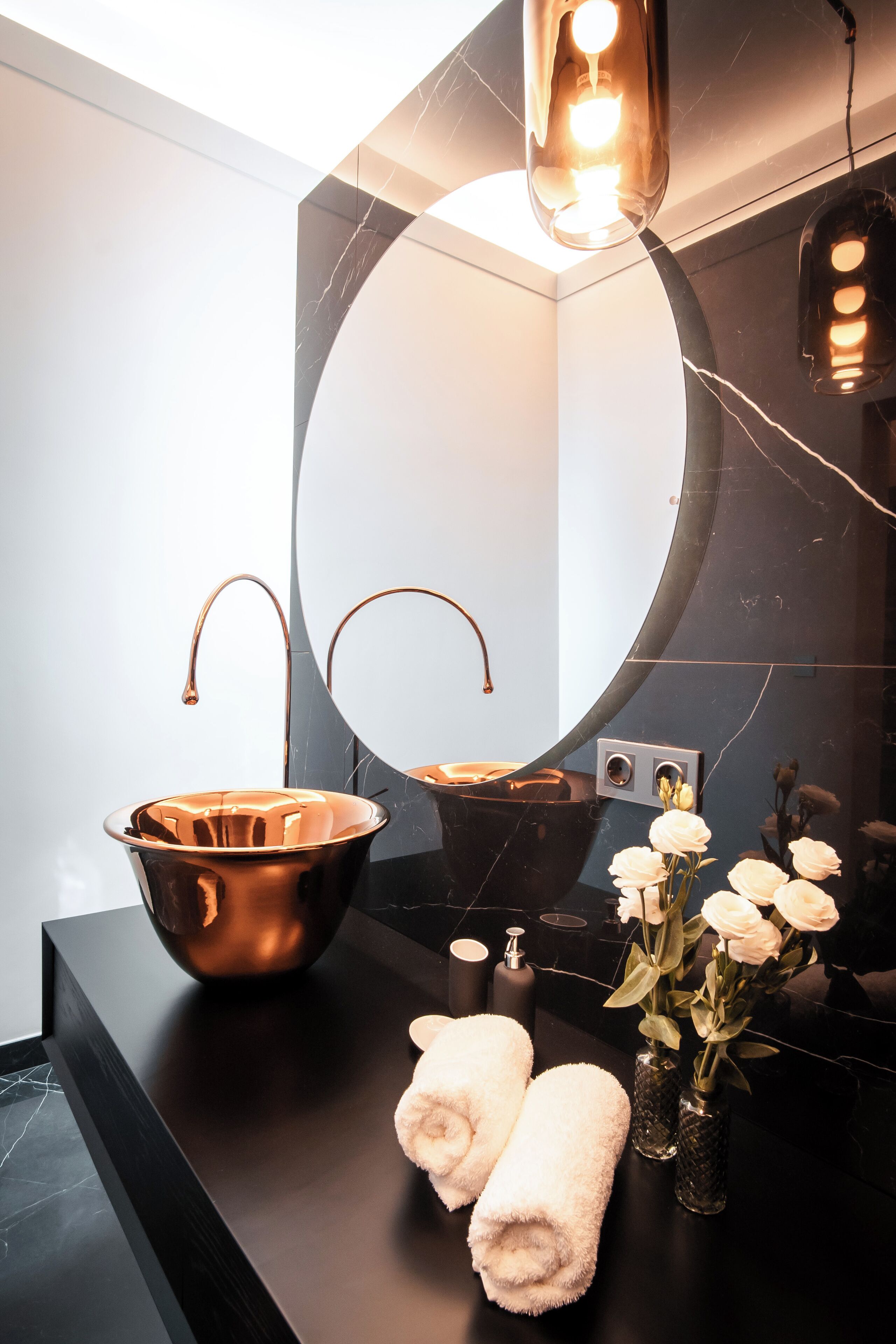 A modern bathroom with a large mirror, a copper sink, and a black countertop.