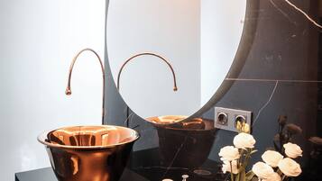 A modern bathroom with a large mirror, a copper sink, and a black countertop.