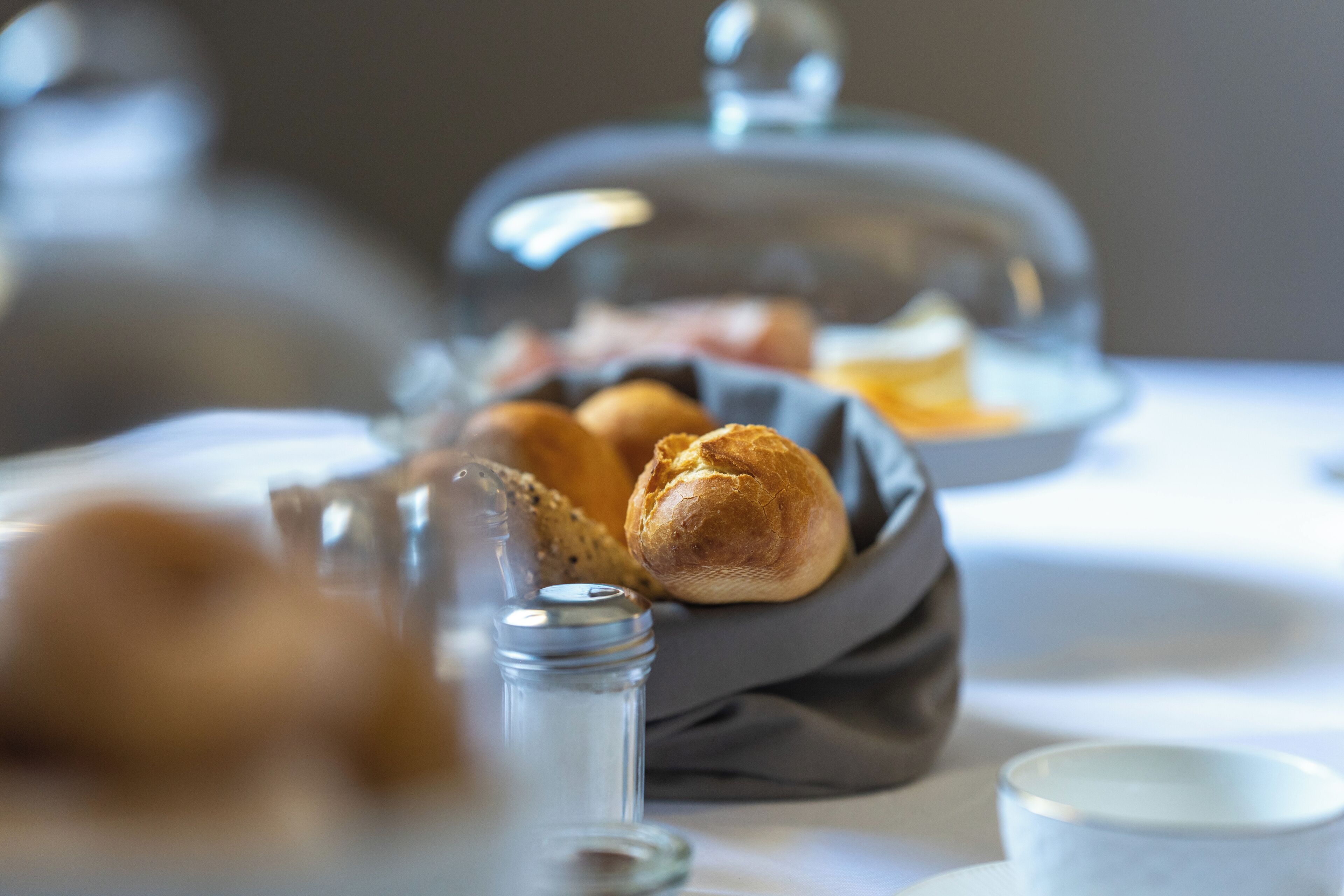 Una mesa con pan, saleros y pimenteros, una taza y una cesta de pan.
