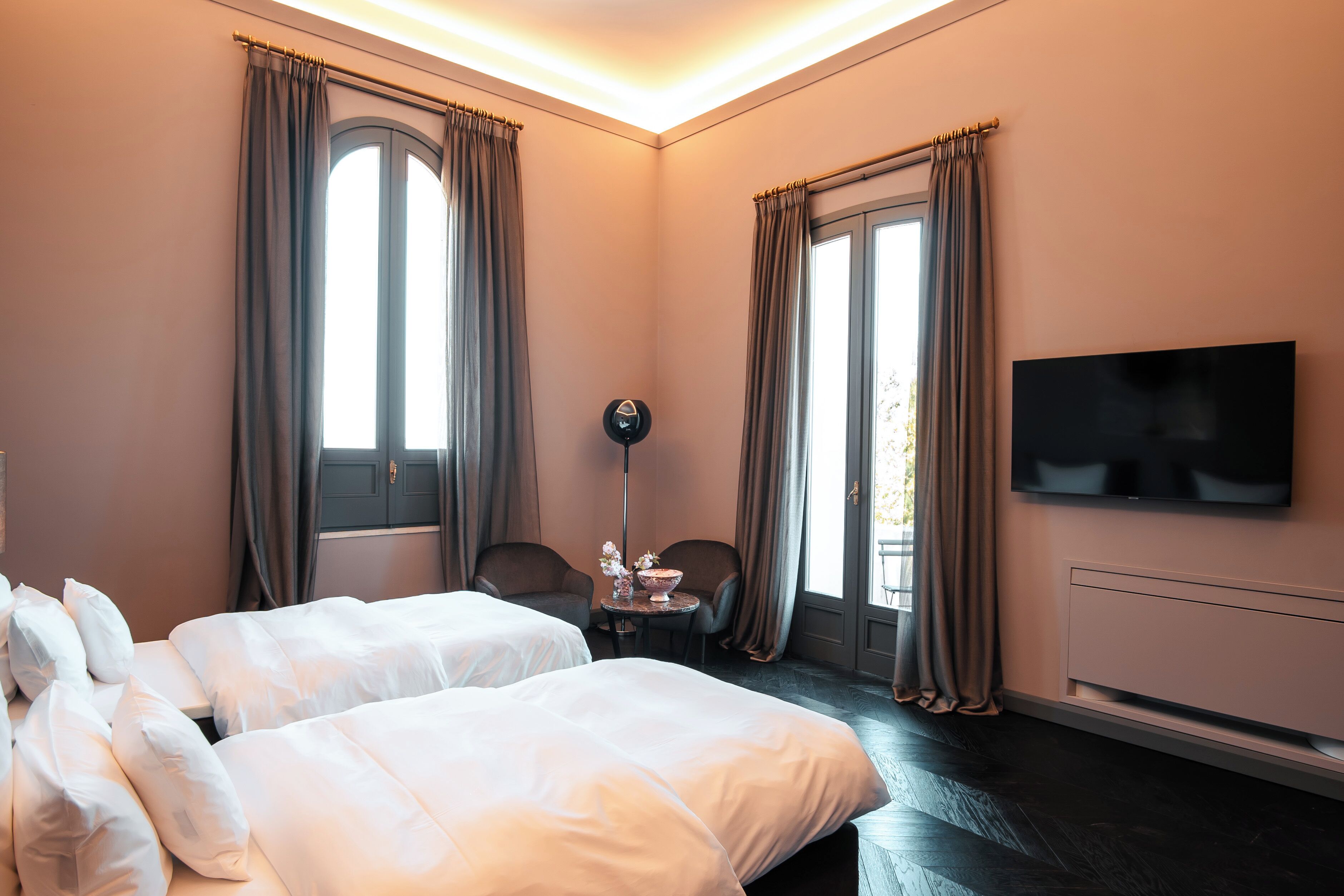 Une chambre d’hôtel avec deux lits, un téléviseur à écran plat, une petite table avec une lampe et une fenêtre avec des rideaux.