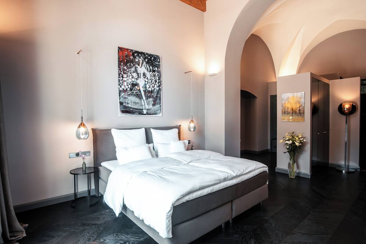 Un dormitorio moderno con una cama grande, dos mesitas de noche, una obra de arte en la pared y un jarrón con flores.