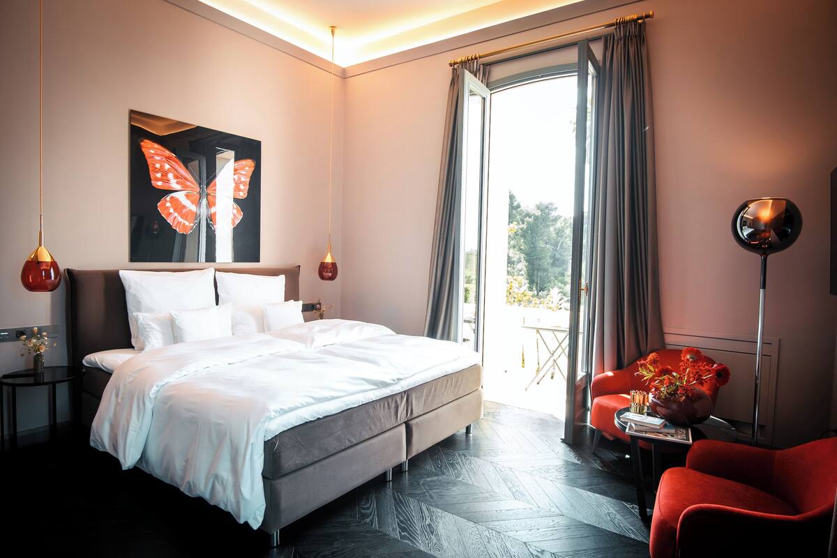 Un dormitorio moderno con una cama grande, un sillón rojo, una lámpara de pie y una obra de arte con mariposas en la pared.