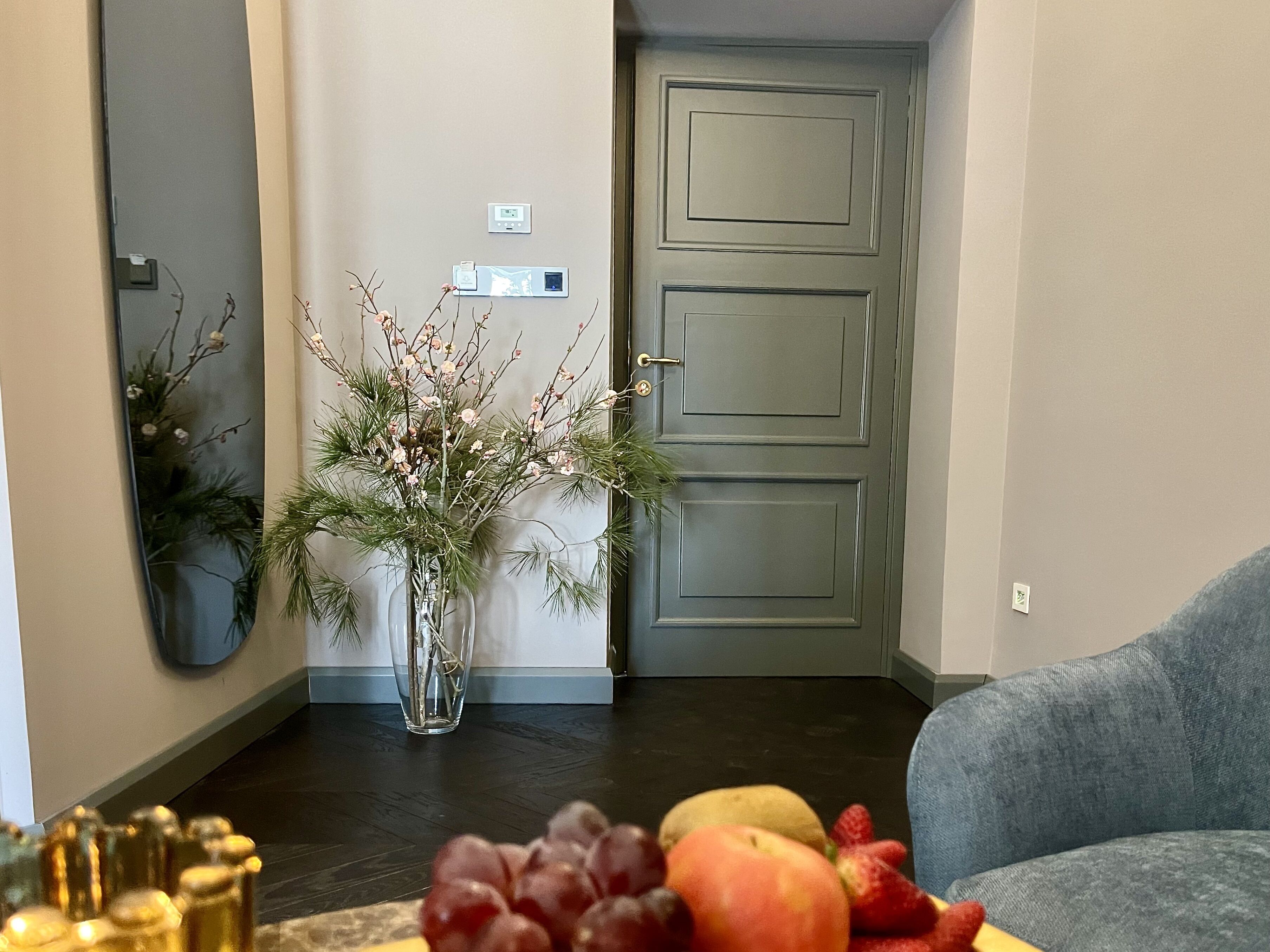A living room with a dark wooden floor, a grey sofa, a vase with flowers, and a fruit bowl.