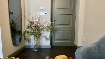 A living room with a dark wooden floor, a grey sofa, a vase with flowers, and a fruit bowl.
