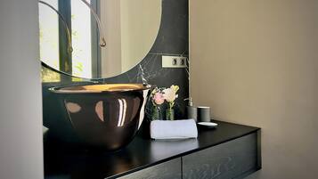 Et moderne badeværelse med et stort spejl, en bordplade i sort marmor, en skålhåndvask, et håndklæde og en vase med blomster.
