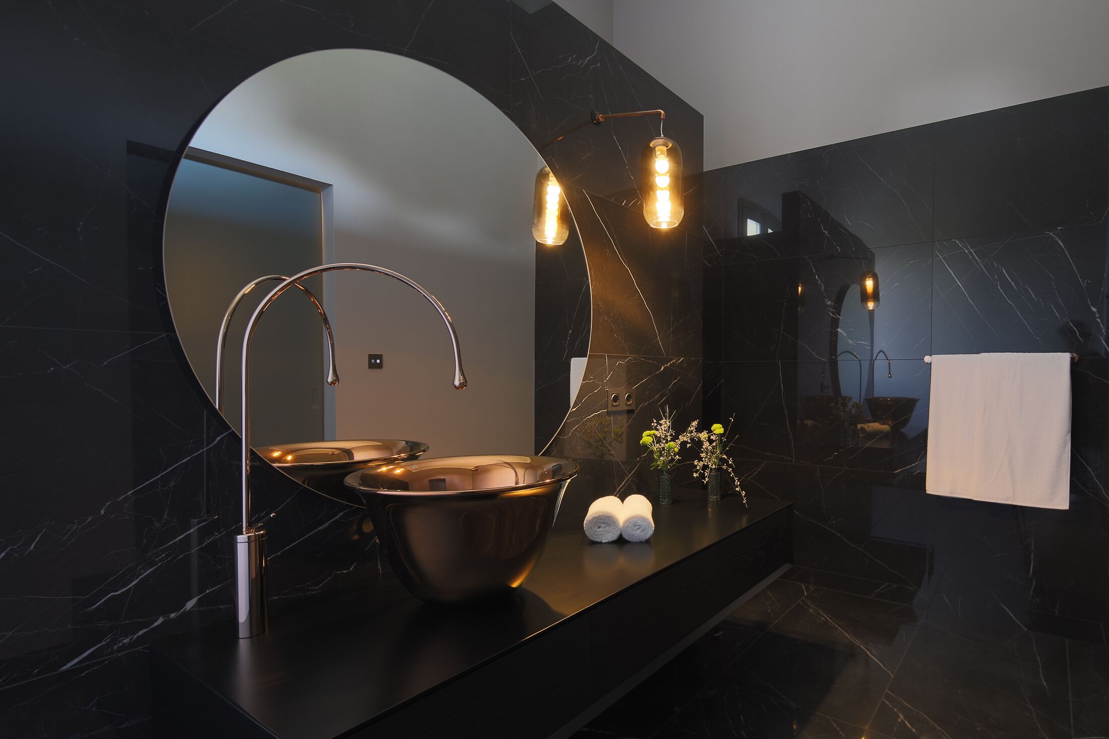 A modern bathroom with a large mirror, a copper sink, and a towel rack.