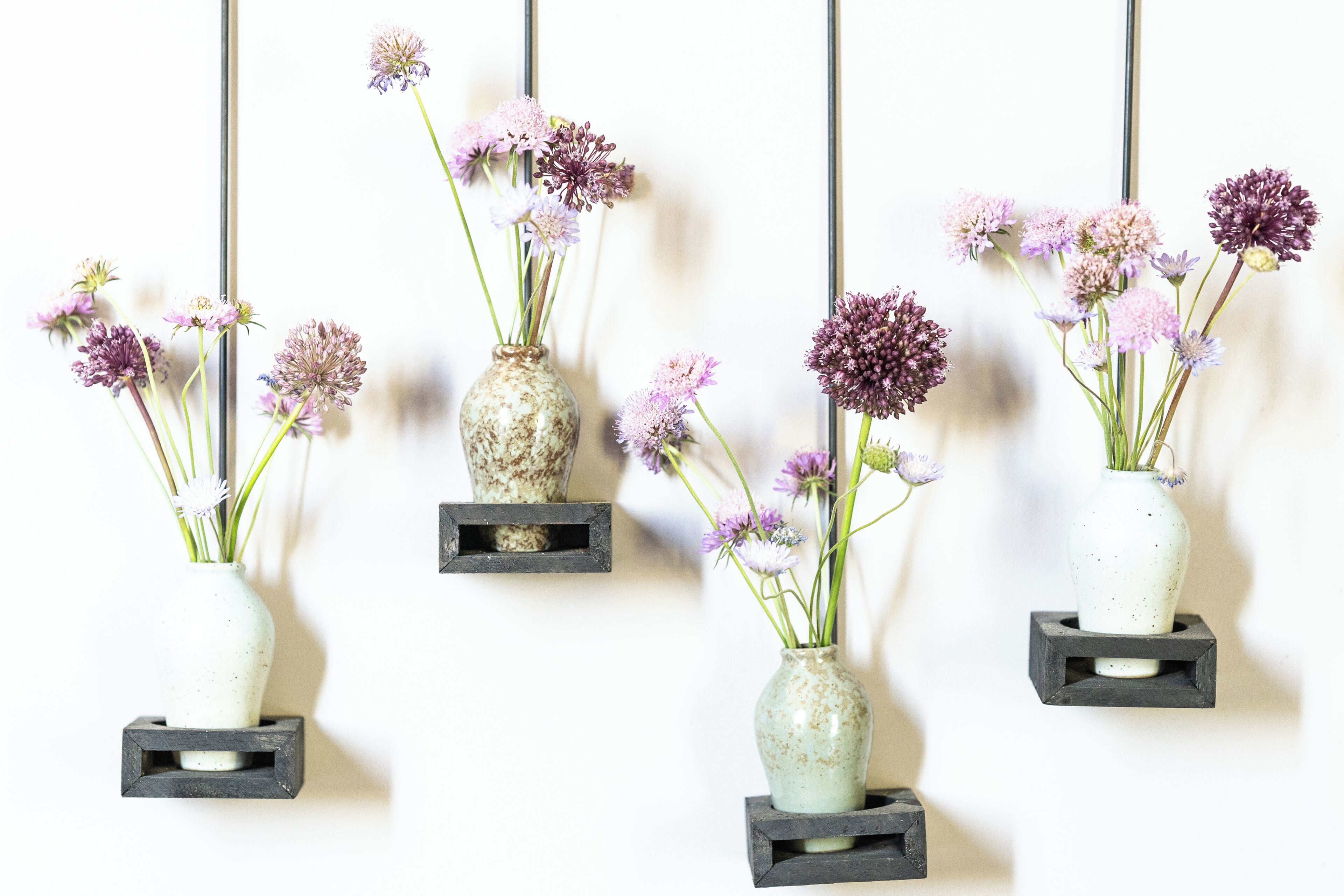 Four wall-mounted vases with flowers, each on a square shelf against a white wall.