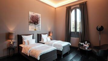 Een hotelkamer met twee bedden, een schilderij, een raam met gordijnen, een stoel, een tafel met een vaas en een vloerlamp.