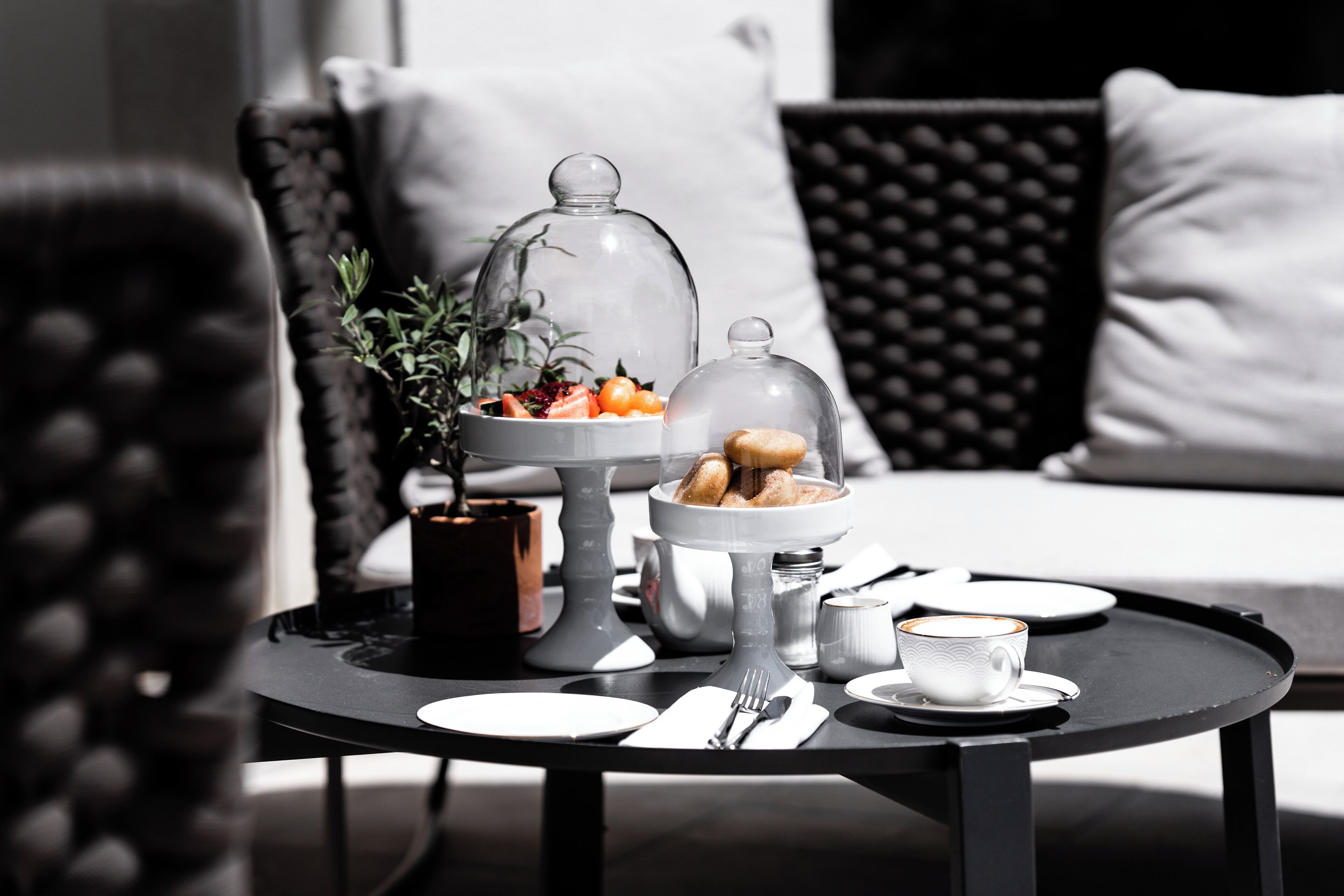 Una mise en place per la colazione con un vassoio coperto di vetro per i dolci, una tazza di caffè e un vassoio con piatti e posate.