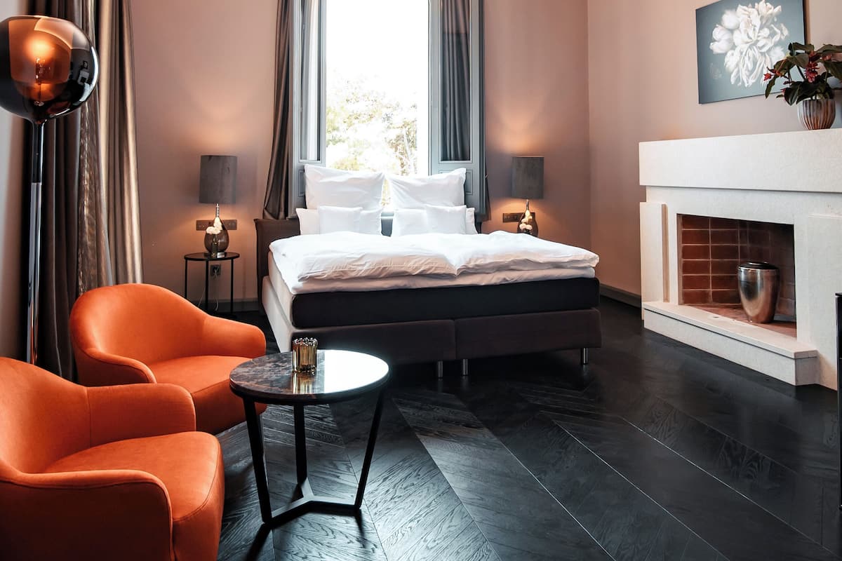 Un dormitorio moderno con una cama grande, dos mesitas de noche, una mesita pequeña y una silla naranja.