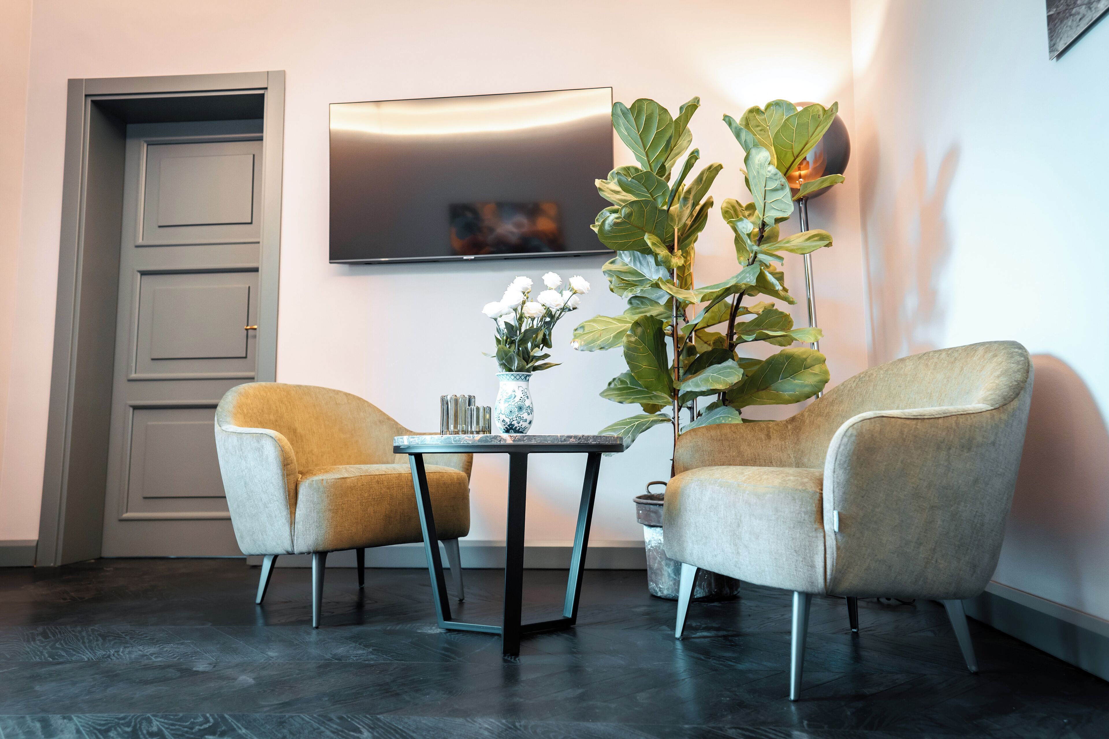 A modern room with two armchairs, a small table, a potted plant, and a flat-screen TV mounted on the wall.