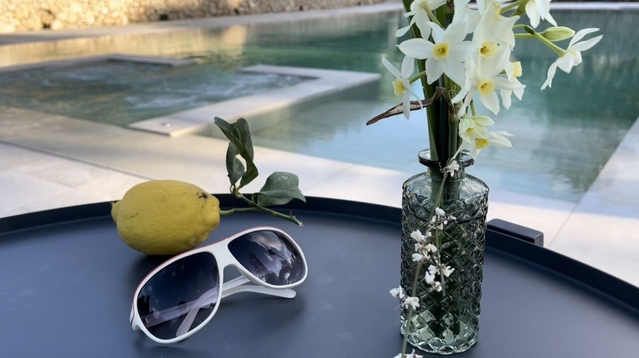 A table with a vase of flowers, a lemon, and sunglasses.