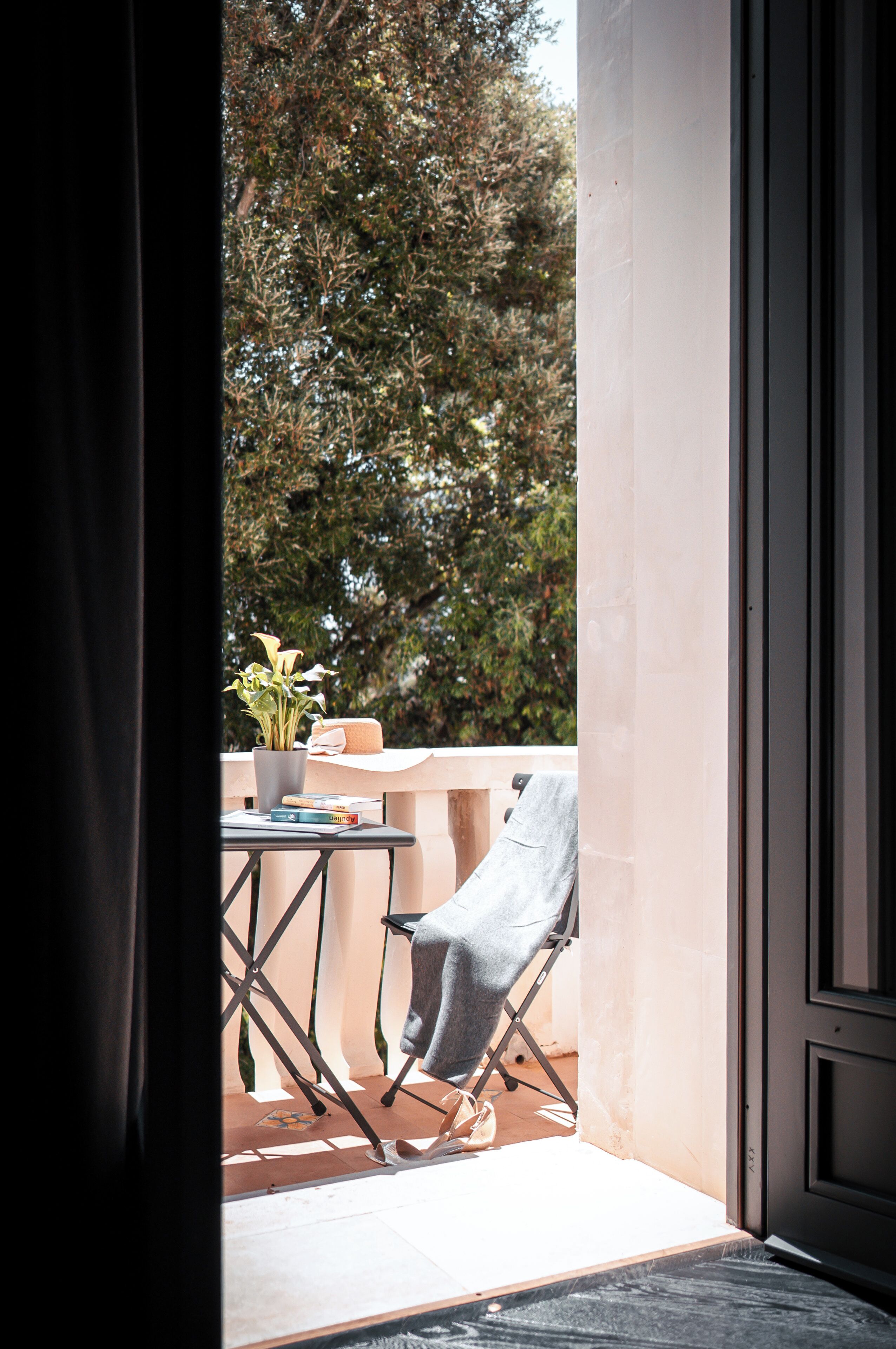 Una porta aperta che dà su un balcone con una sedia, un tavolo e una pianta in vaso.