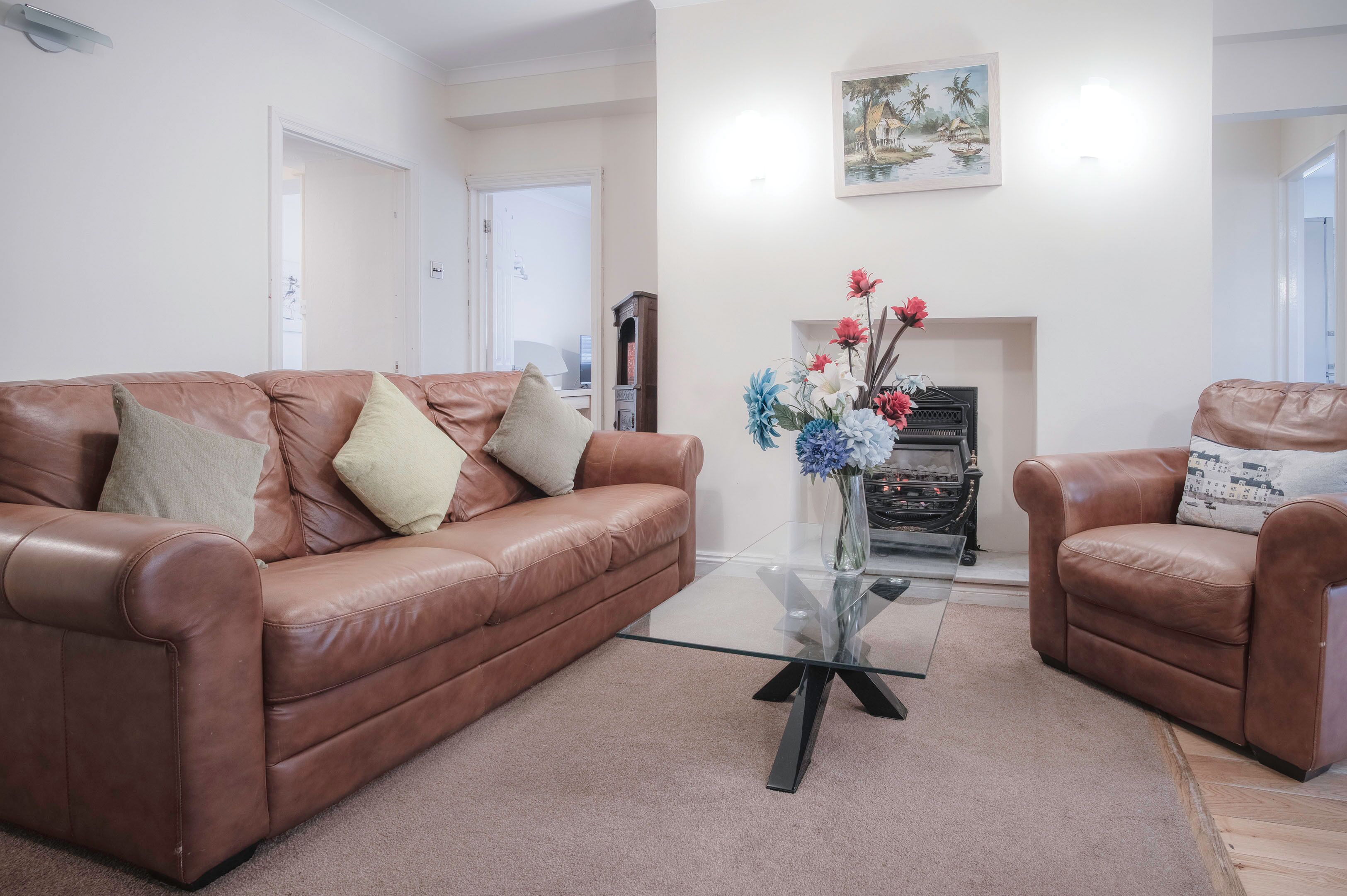 A living room with a brown leather sofa, a glass coffee table, and a vase of flowers.