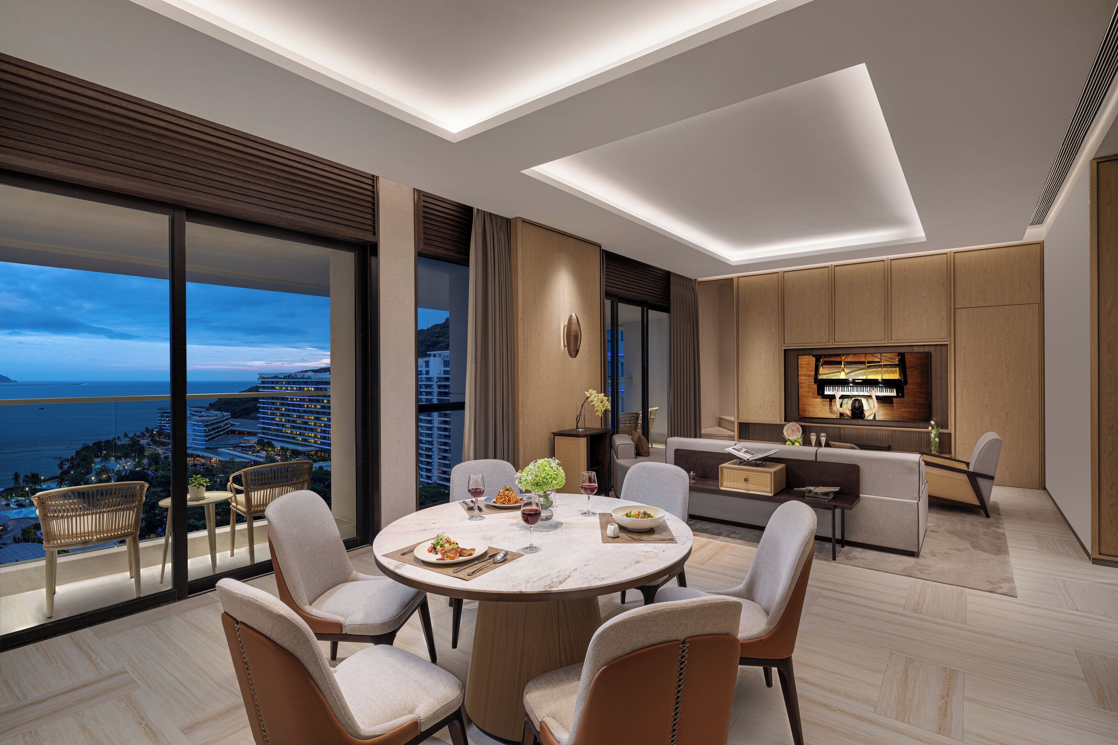 Une chambre d’hôtel moderne dotée d’un coin repas, d’une cuisine et d’une grande fenêtre offrant une vue sur la ville et la mer.