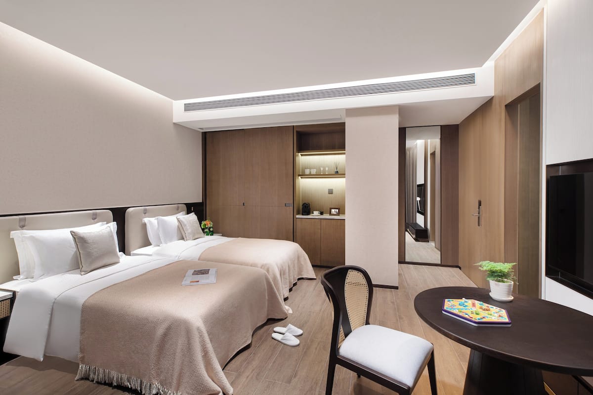 Ein modernes Hotelzimmer mit zwei Betten, einem Esstisch, einem Stuhl, einem Fernseher und einer kleinen Küchenzeile.