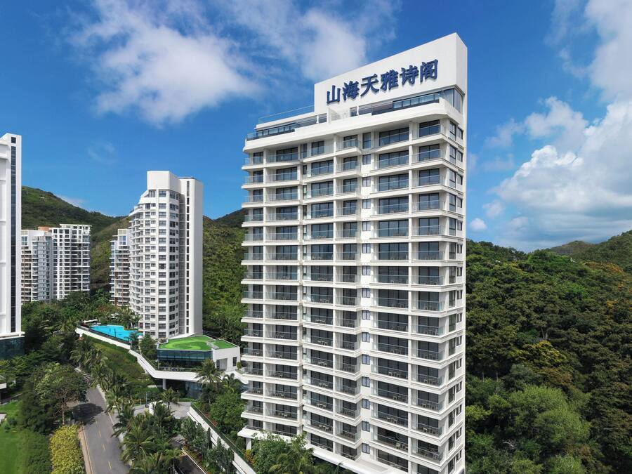 A modern hotel with multiple floors, surrounded by lush greenery and hills.