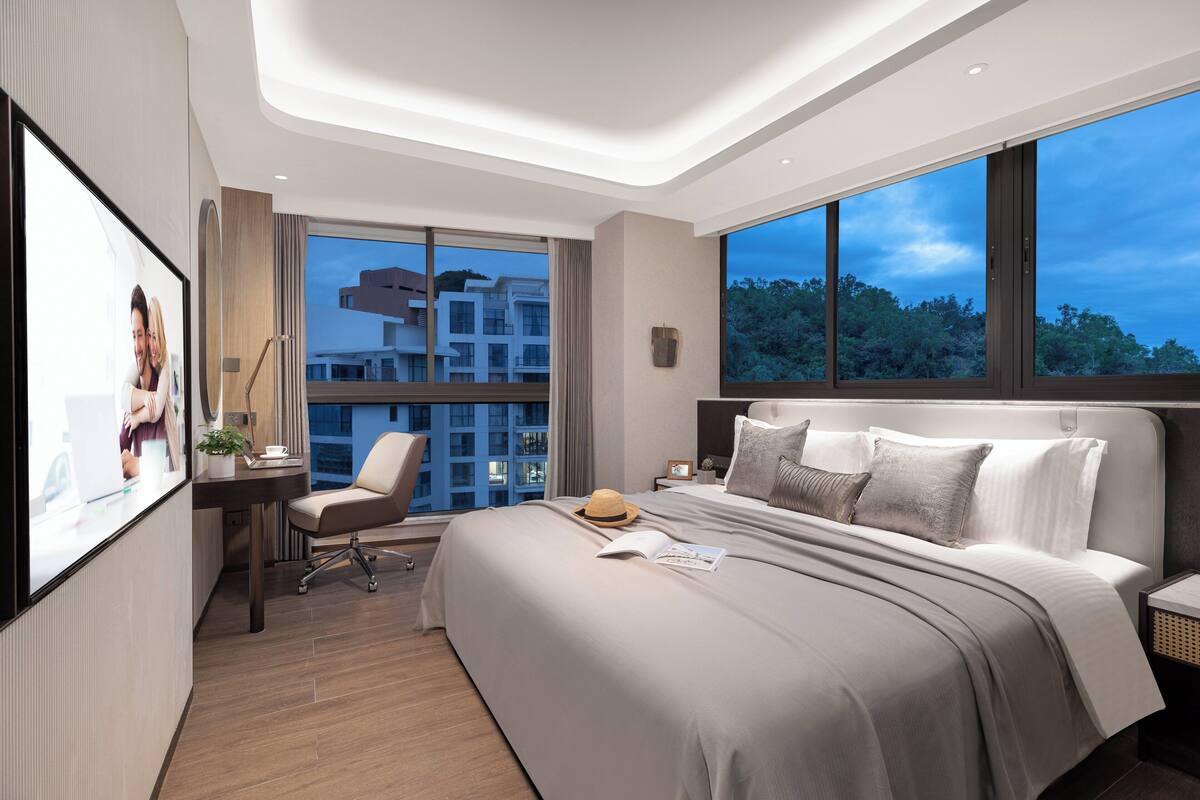 Ein modernes Hotelzimmer mit einem großen Bett, einem Schreibtisch und einem Stuhl. Ein großes Fenster bietet Blick auf Gebäude und Bäume.
