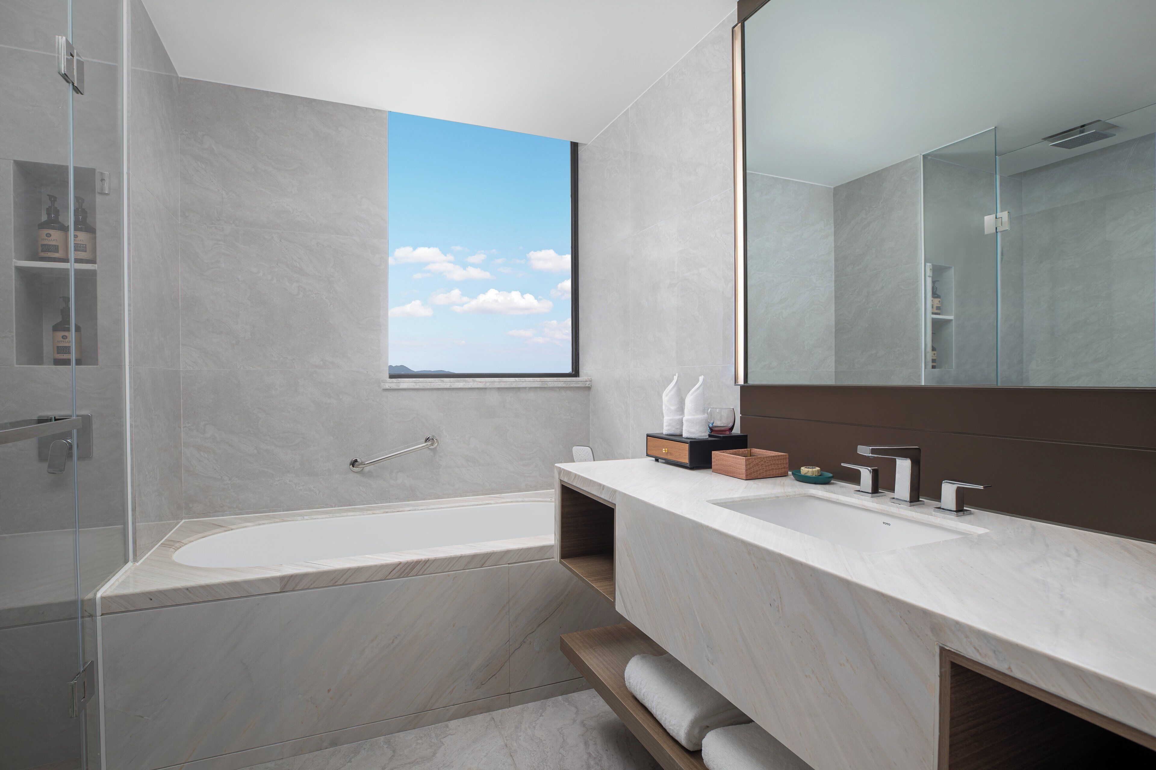 A modern bathroom with a large bathtub, a vanity with a mirror, and a window providing a view of the sky.