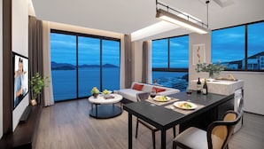 Ein modernes Hotelzimmer mit Essbereich, großen Fenstern mit Meerblick, einer Couch und einer kleinen Küchenzeile.
