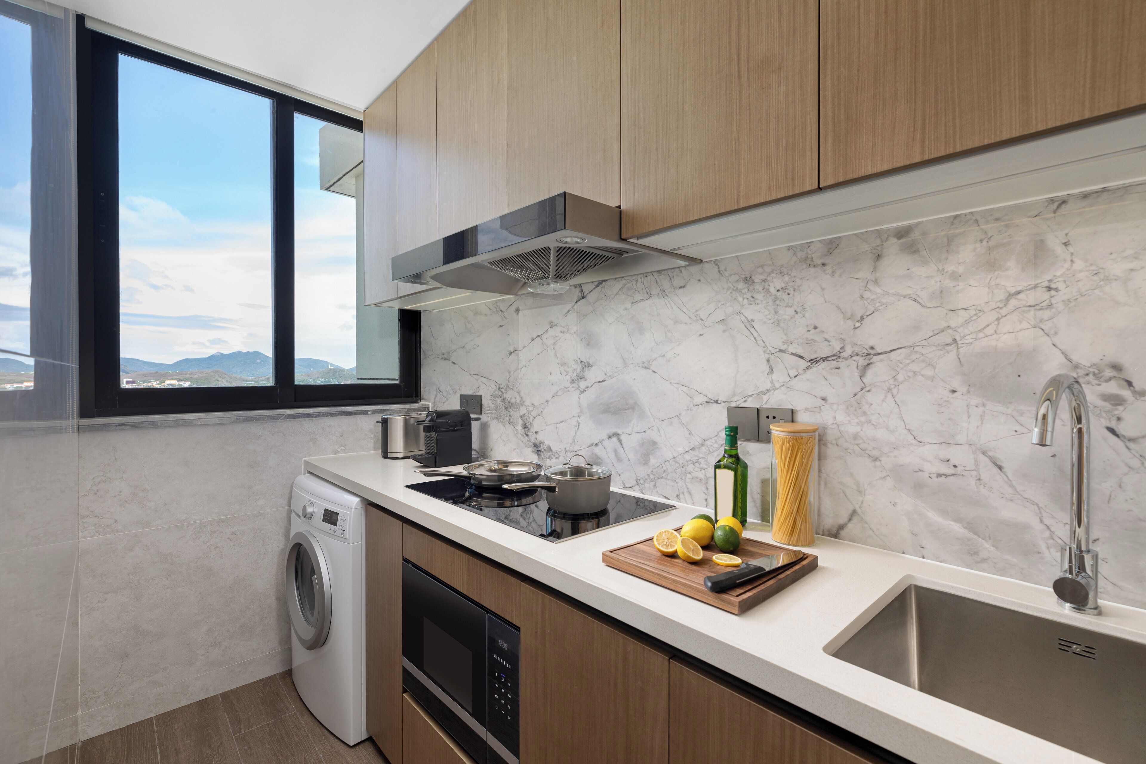 Cocina moderna con lavadora incorporada, estufa, pileta y ventana con vista a un paisaje montañoso.
