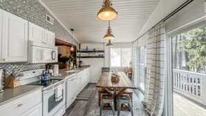 A kitchen with white cabinets, a wooden dining table, and pendant lighting.