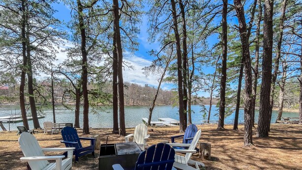 A lakeside campsite with Adirondack chairs, a fire pit, and a view of the lake.