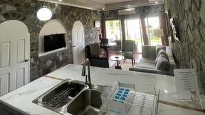 A kitchen with a stone wall, a built-in TV, and a dining area with a sofa and chairs. - Stonetrail (Villa)
