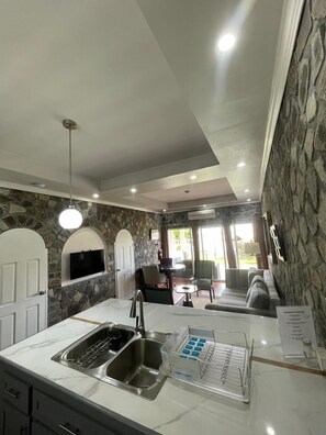 A kitchen with a stone wall, a built-in TV, and a dining area with a sofa and chairs. - Stonetrail (Villa)