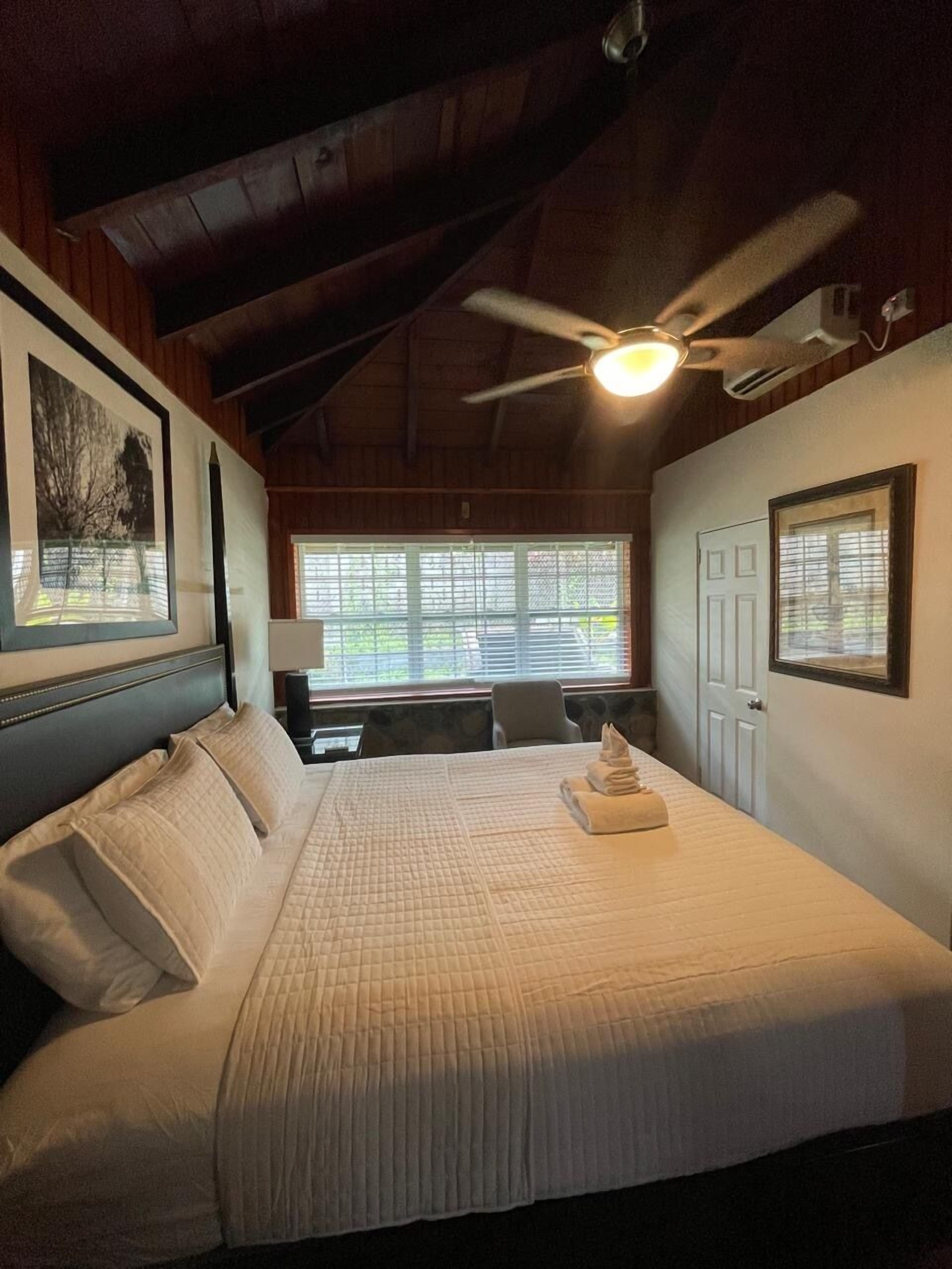 Un dormitorio con cama, ventilador de techo, escritorio y ventana.