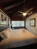 Un dormitorio con cama, ventilador de techo, escritorio y ventana.