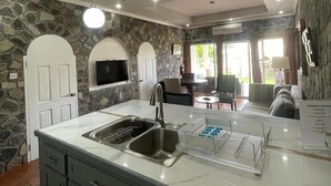 A modern kitchen with a stone wall backsplash, a built-in sink, and a dining area with a table and chairs. - Stonetrail (Villa)