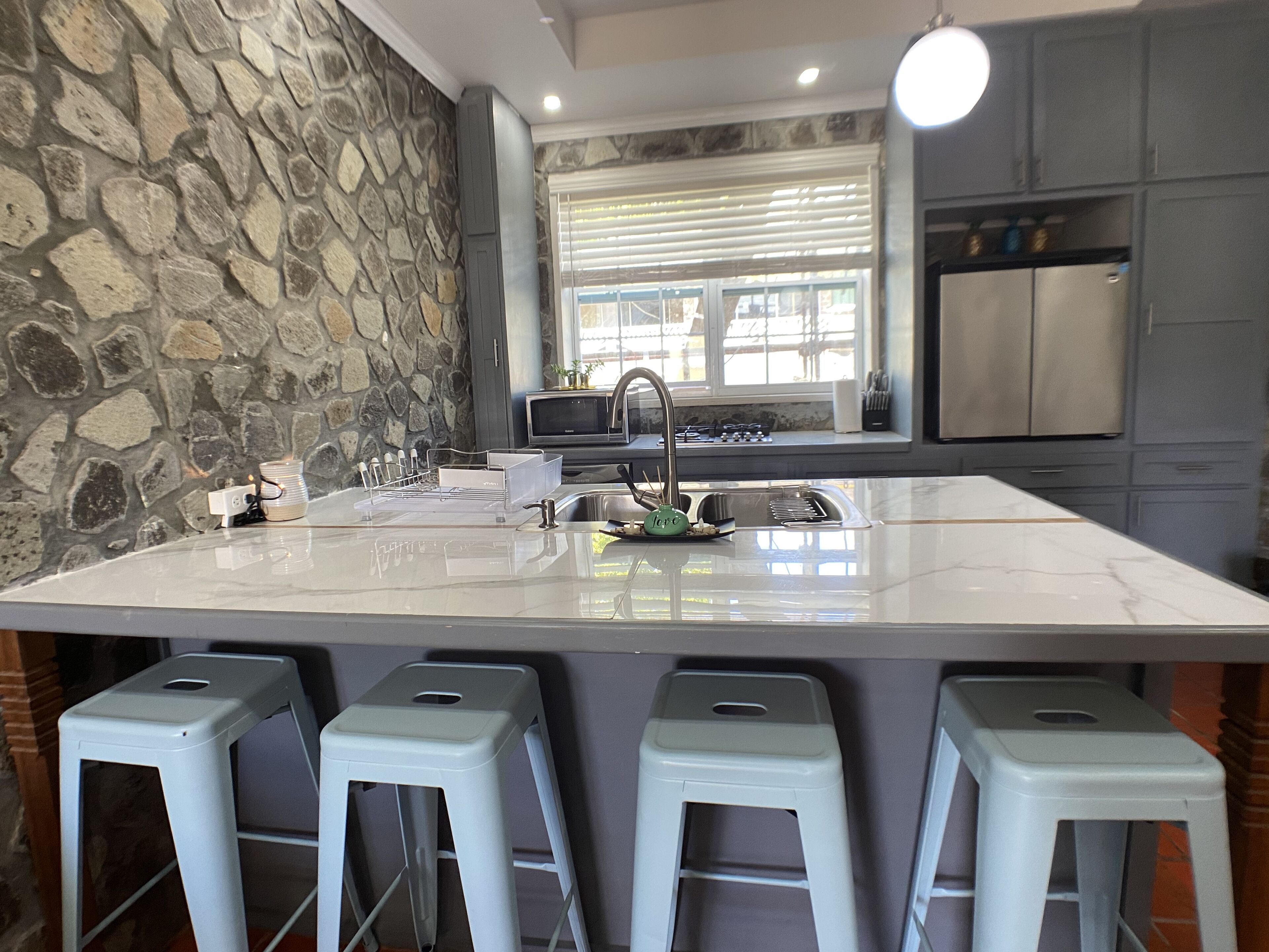 A kitchen with a large island, stone wall, modern appliances, and bar stools.