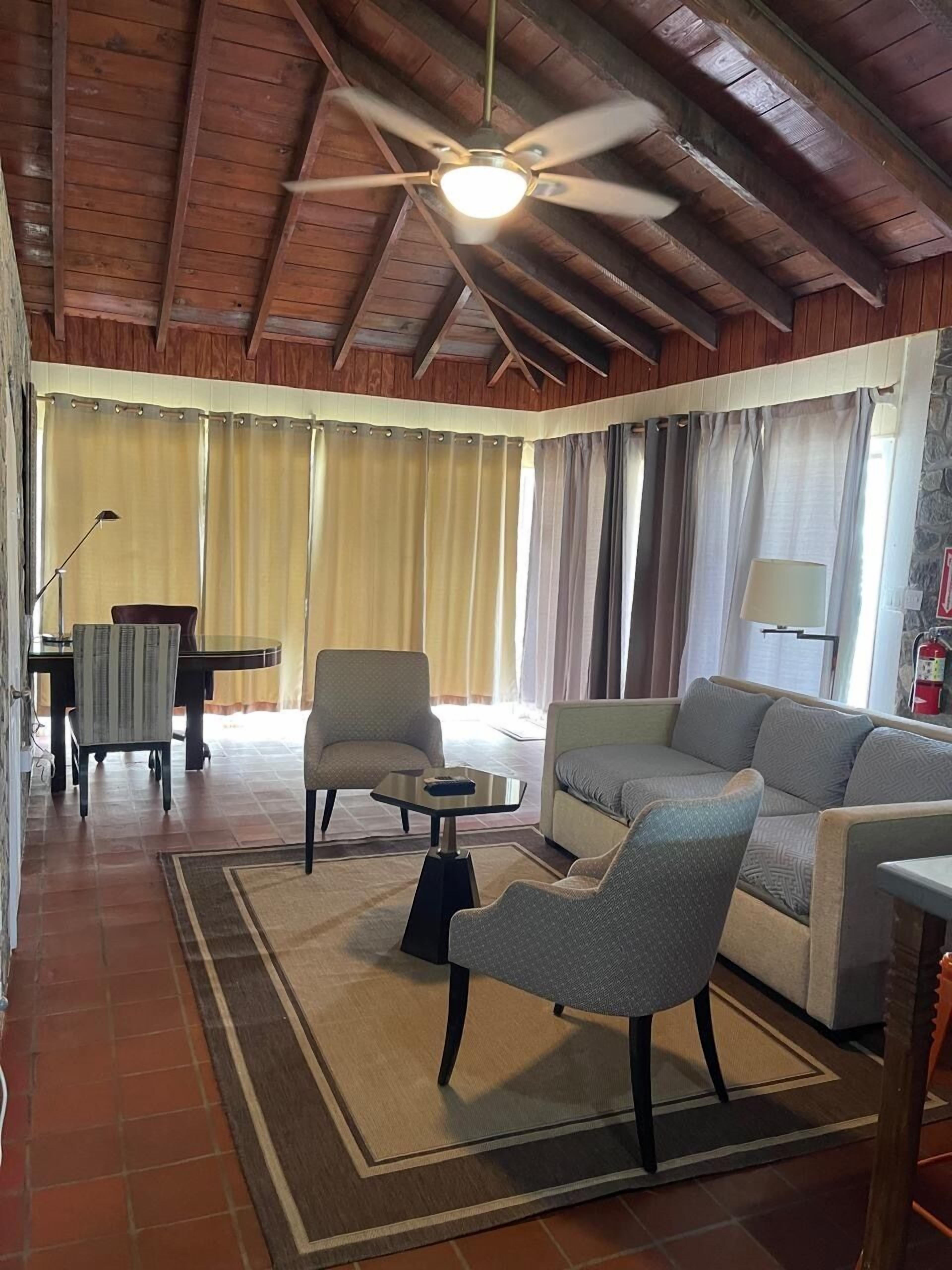 Zona d'estar àmplia amb ventilador de sostre, un sofà, butaques, una taula de cafè i una taula de dinar amb cadires.