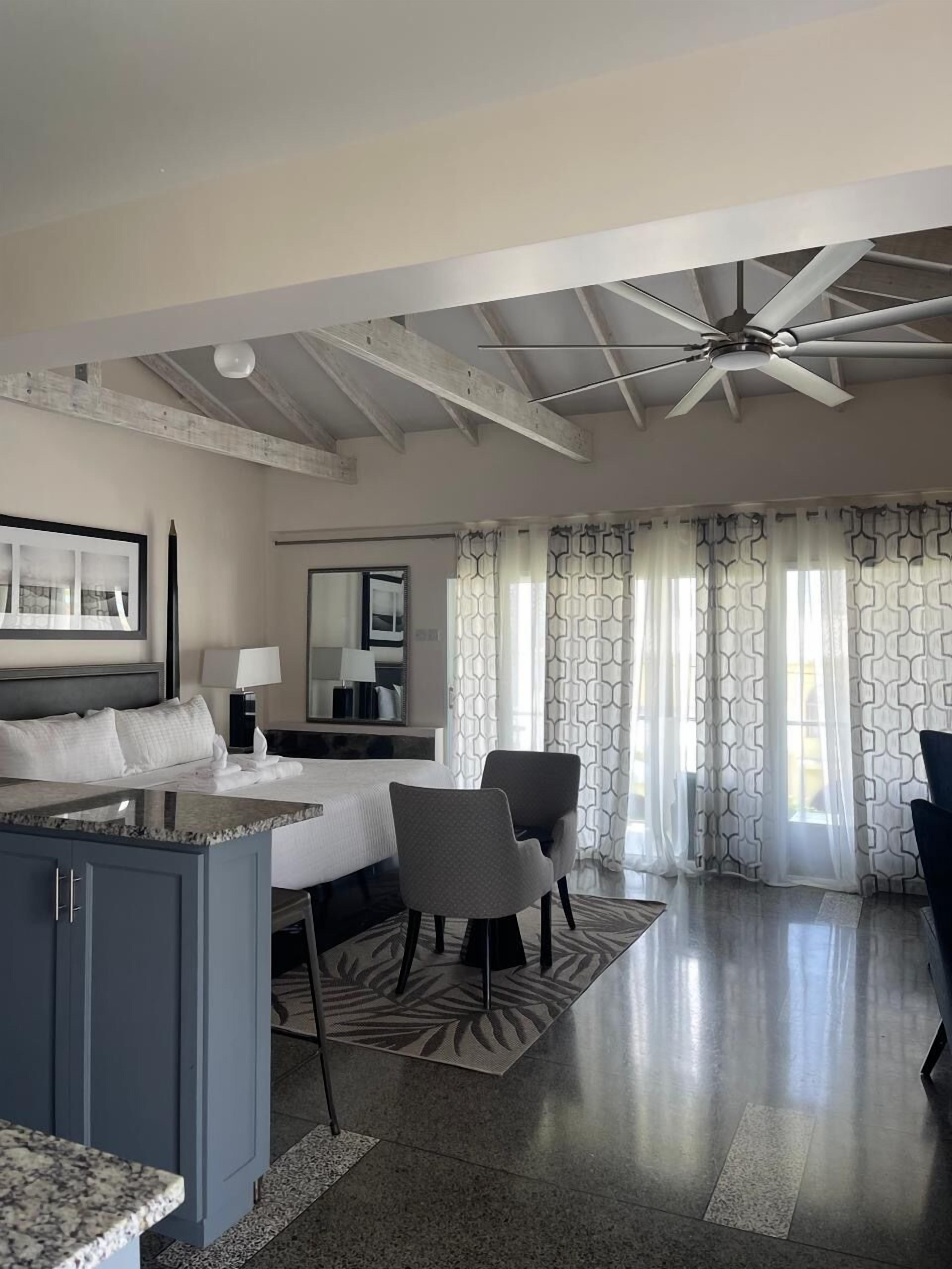 Habitación de hotel con cama, escritorio, sillas, ventilador de techo y cortinas estampadas.
